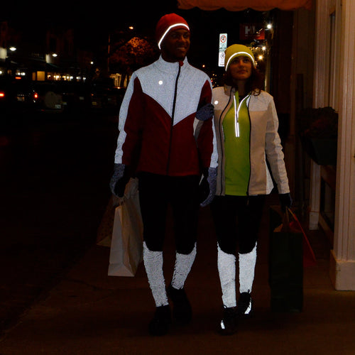 A man and a woman walking on a sidewalk wearing reflective pants and jackets